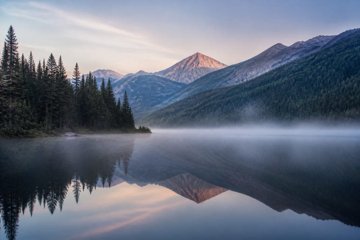 A still mountain lake at dawn with mist on the water